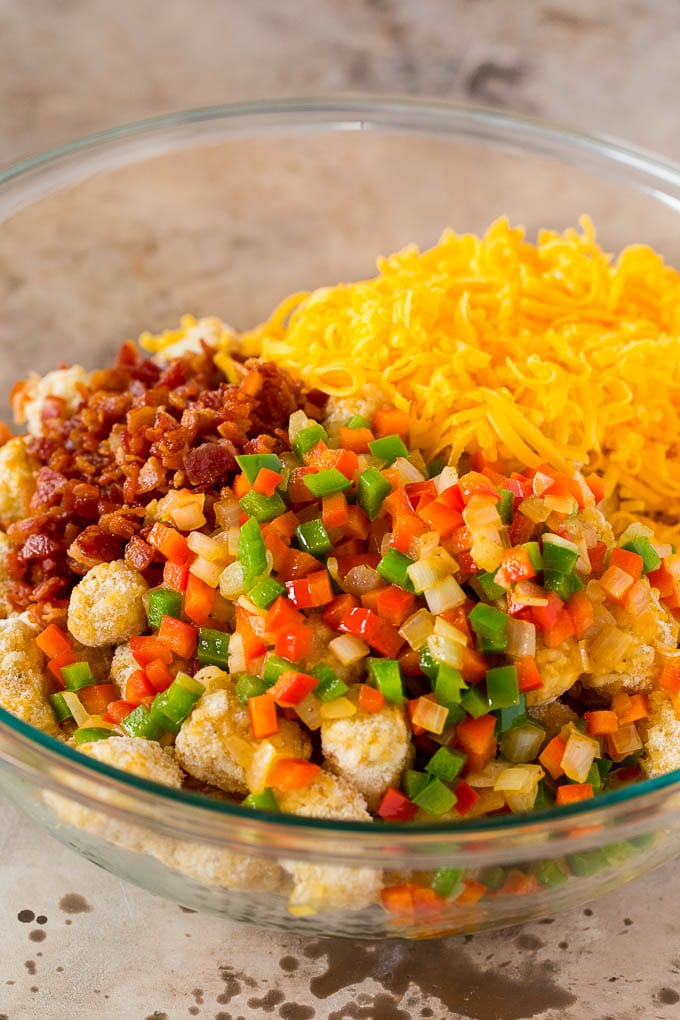 A bowl of frozen tater tots, vegetables, bacon and shredded cheese.