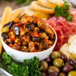 A bowl of eggplant caponata served with olives, cured meats and bread.