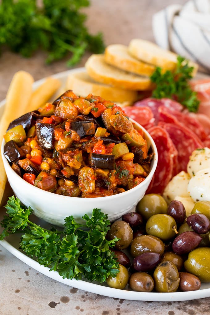A bowl of eggplant caponata served with olives, cured meats and bread.