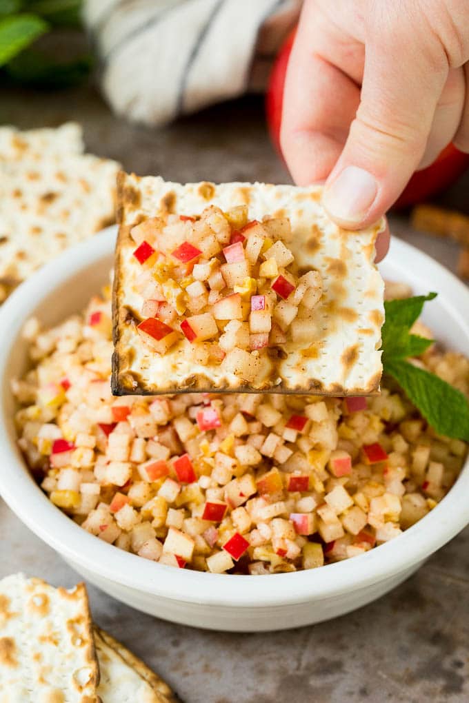 A hand holding a piece of matzo with a serving of charoset on top.