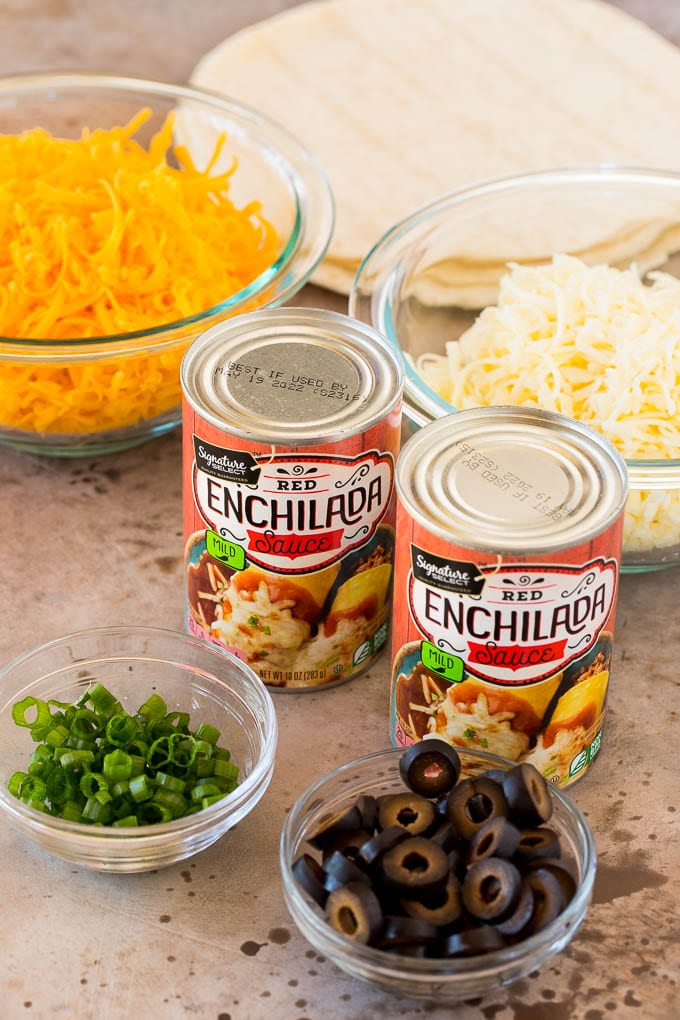 Cans of sauce and bowls of shredded cheese, green onions and olives.