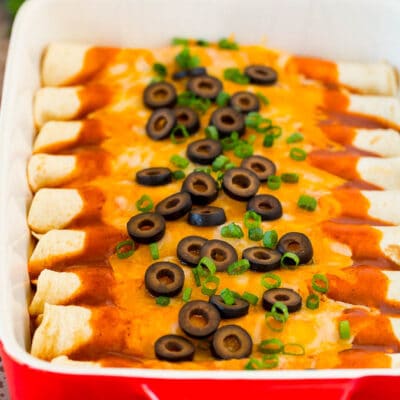 A dish of cheese enchiladas topped with olives and green onions.