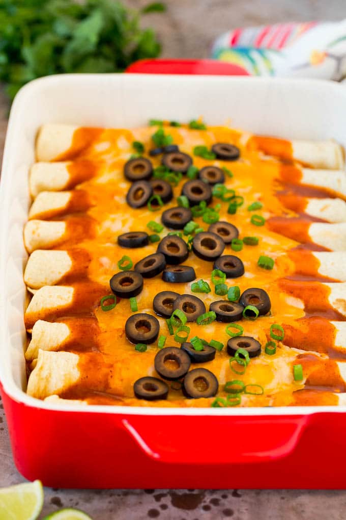 A dish of cheese enchiladas topped with olives and green onions.