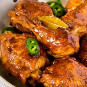 A pan of chicken adobo garnished with sliced jalapeno.