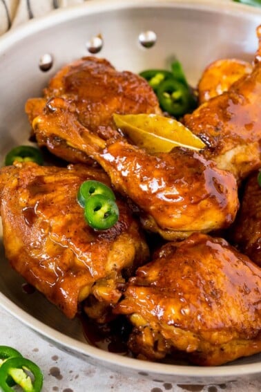 A pan of chicken adobo garnished with sliced jalapeno.
