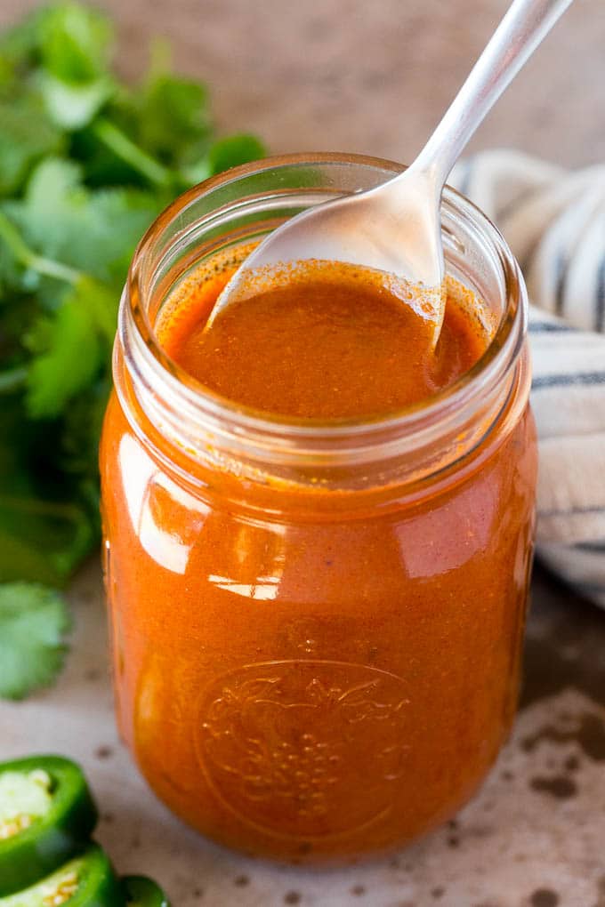 A jar of homemade enchilada sauce with a spoon in it.