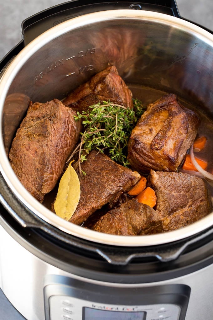 A pressure cooker with short ribs, herbs, vegetables and beef broth.