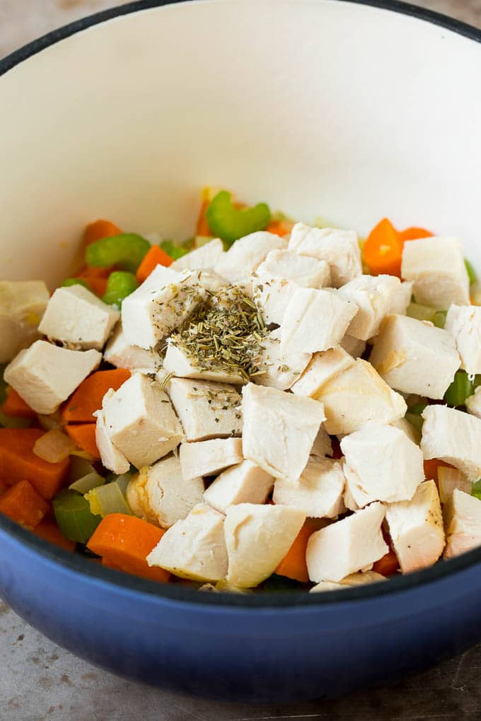 Diced chicken and herbs in a pot with vegetables.