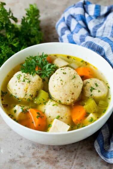A bowl of matzo ball soup with chicken, garnished with parsley.