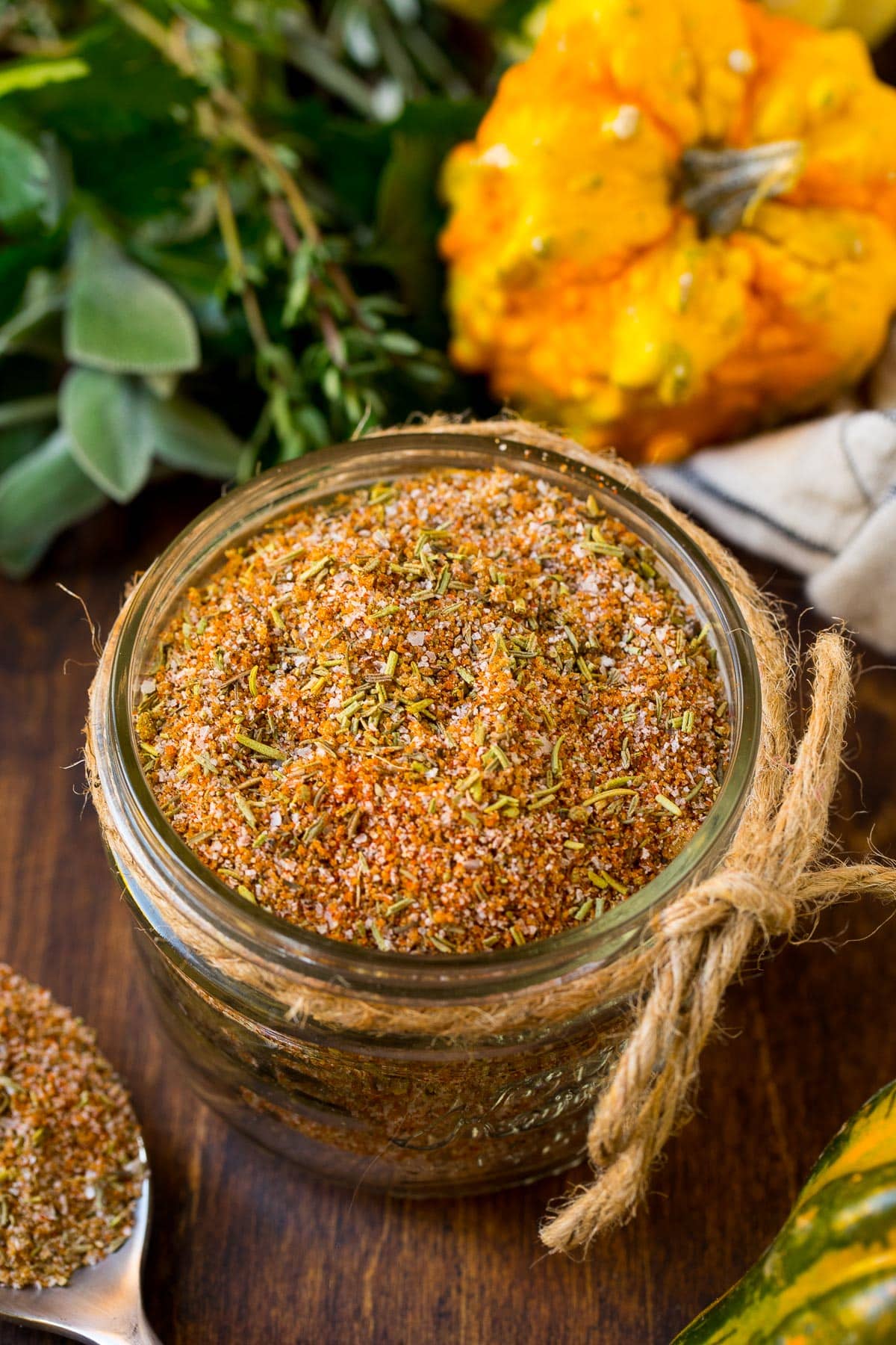 A jar of turkey rub surrounded by squash and herbs.