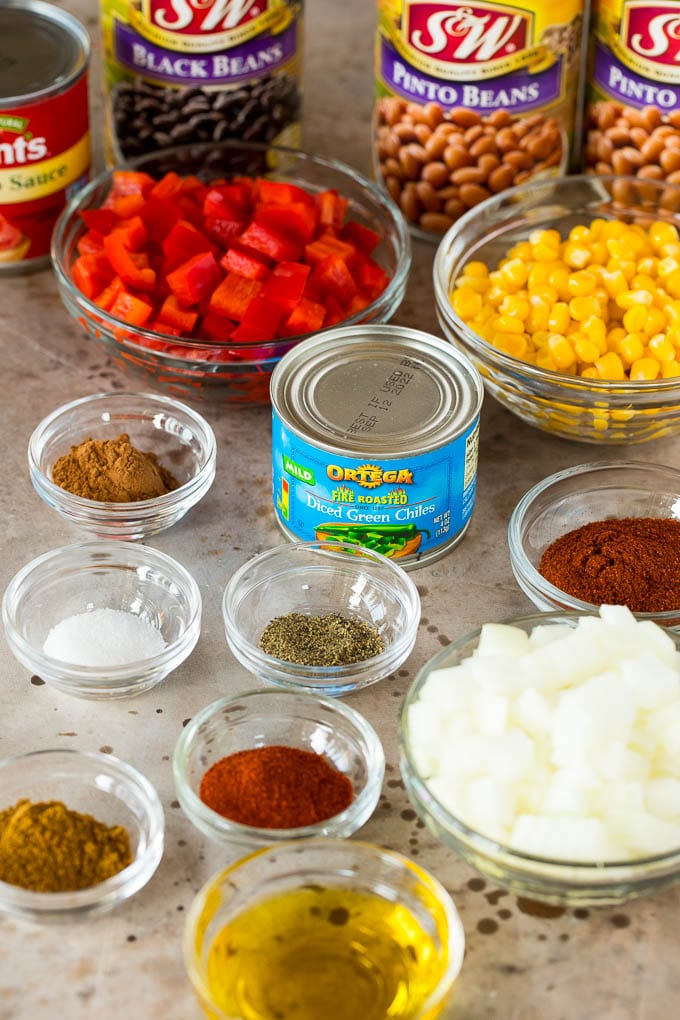 Chili ingredients in glass bowls including spices and vegetables.