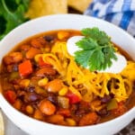 A bowl of vegetarian chili topped with shredded cheese and sour cream.
