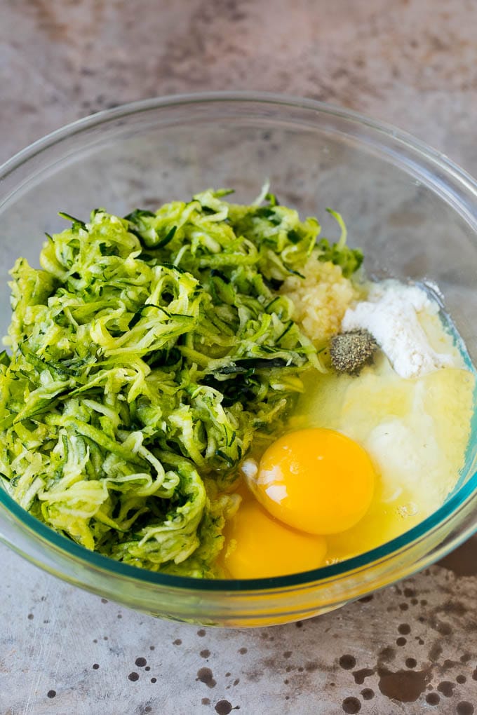 Zucchini, flour, eggs and seasonings in a bowl.