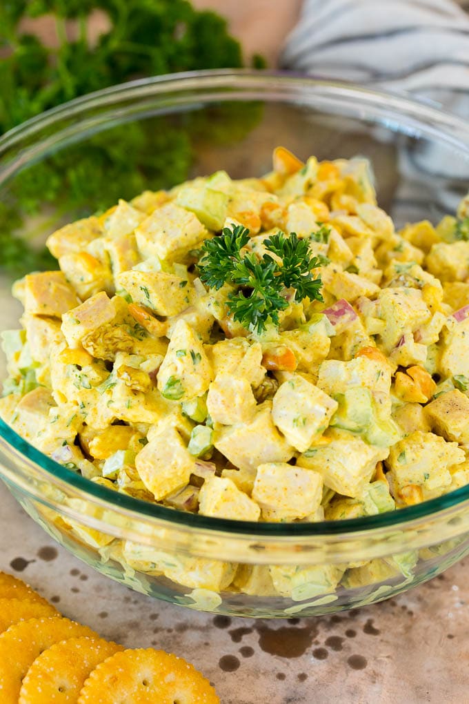 A serving bowl of curry chicken salad garnished with parsley.