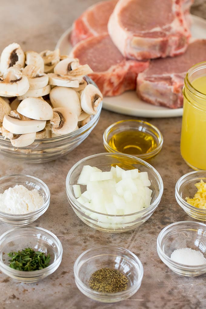 Pork chops, onions, mushrooms and seasonings in bowls.