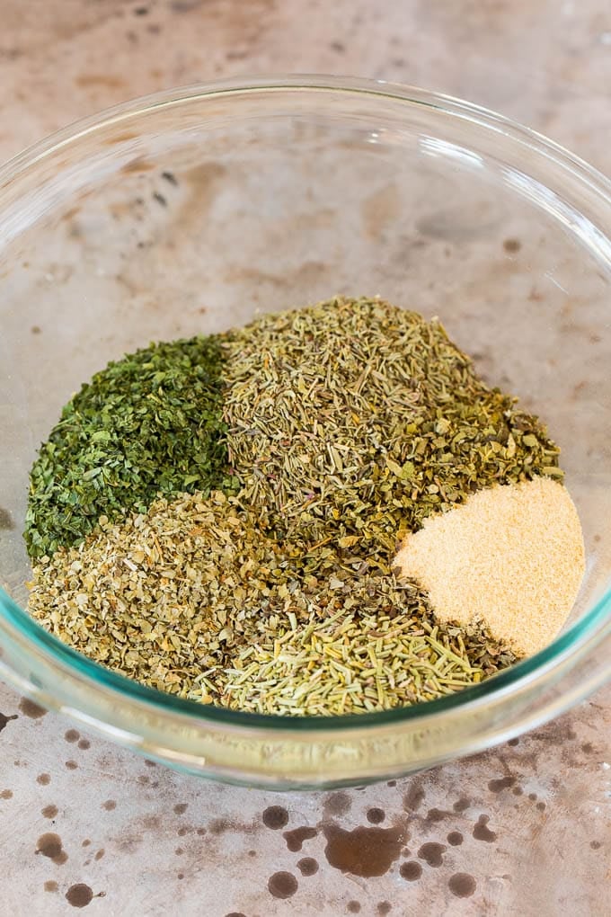 A mixing bowl with dried herbs and garlic powder in it.