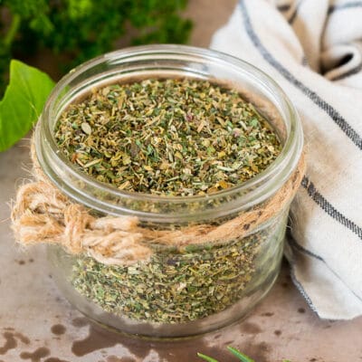 A jar of homemade Italian seasoning surrounded by fresh herbs.