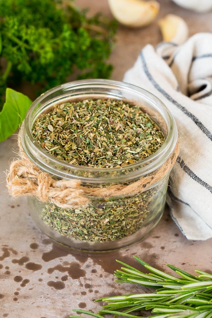 A jar of homemade Italian seasoning surrounded by fresh herbs.