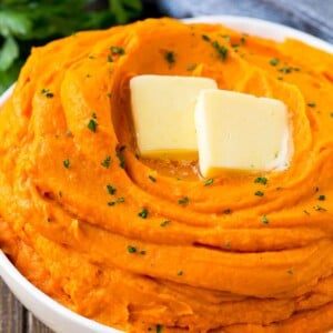 A bowl of mashed sweet potatoes topped with butter and parsley.