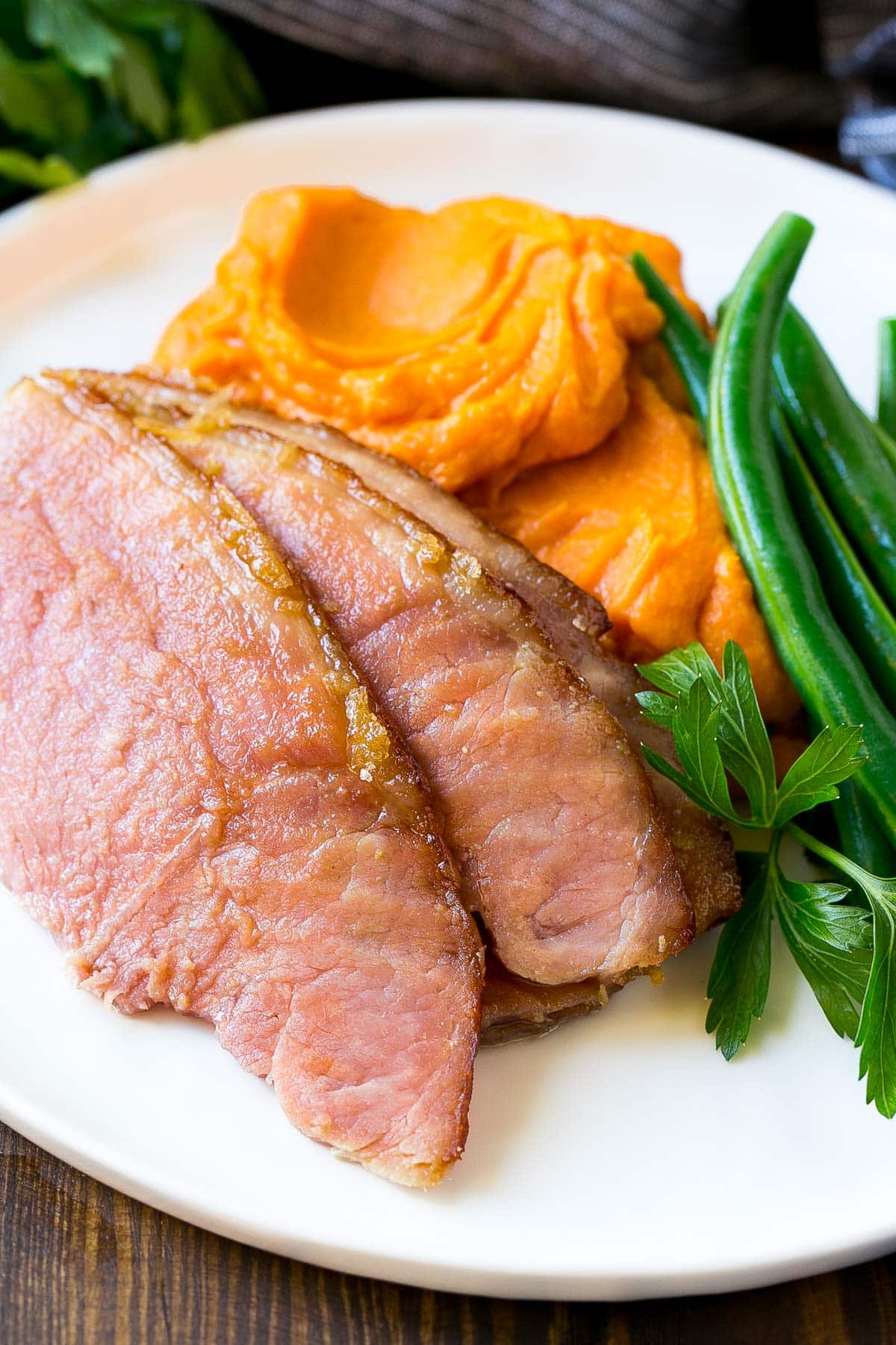 Sliced ham on a plate with mashed sweet potatoes and green beans.