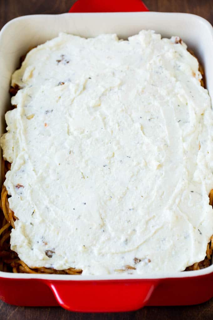 Ricotta cheese spread over spaghetti in a baking dish.