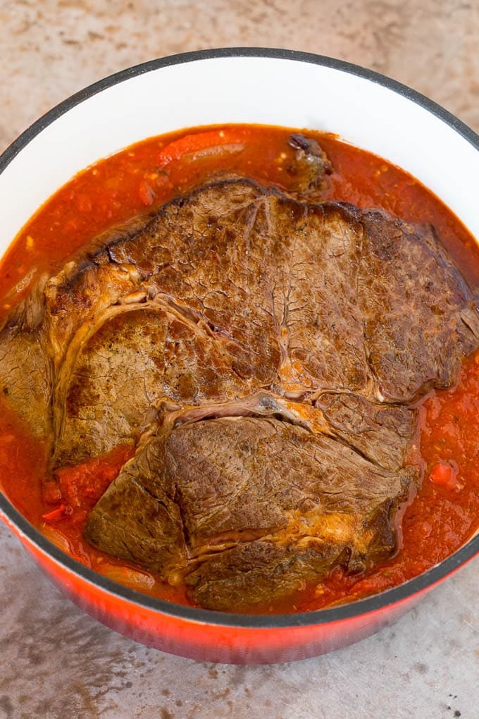 A seared roast in a pot of tomato and pepper sauce.