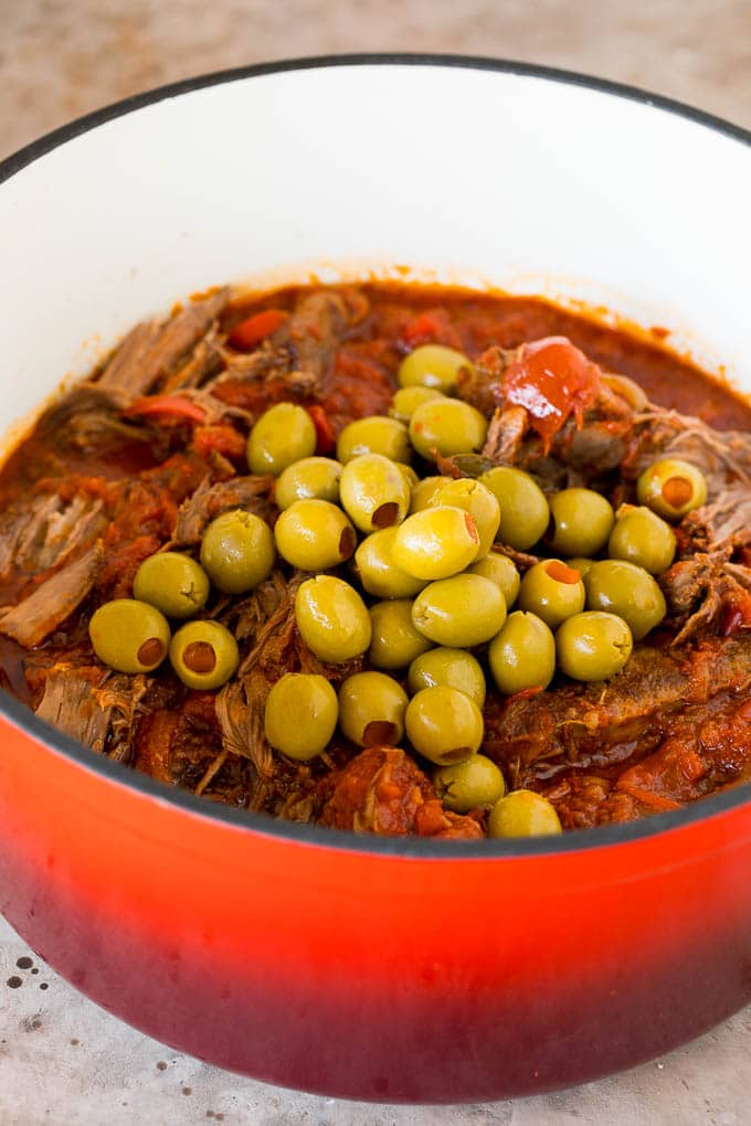 A pot of shredded beef with whole green olives on top.