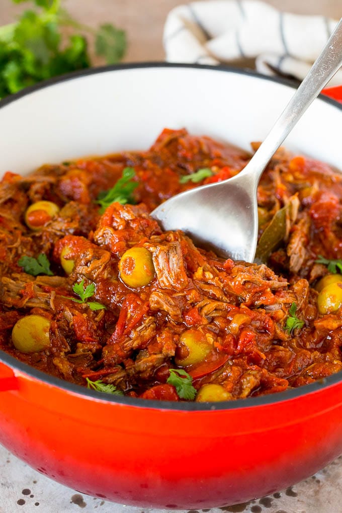 A serving spoon in a pot of ropa vieja with a garnish of cilantro.