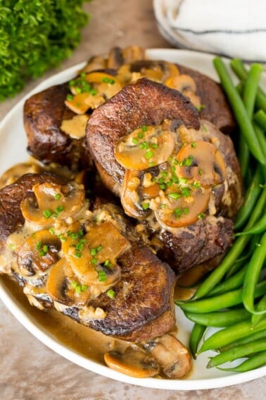 A plate of Steak Diane topped with mushroom sauce and served with green beans.