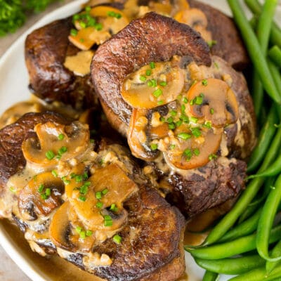 A plate of Steak Diane topped with mushroom sauce and served with green beans.