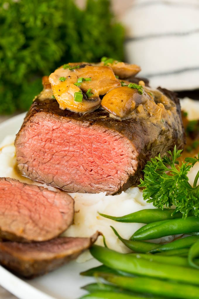 Sliced Steak Diane served with mashed potatoes and green beans.