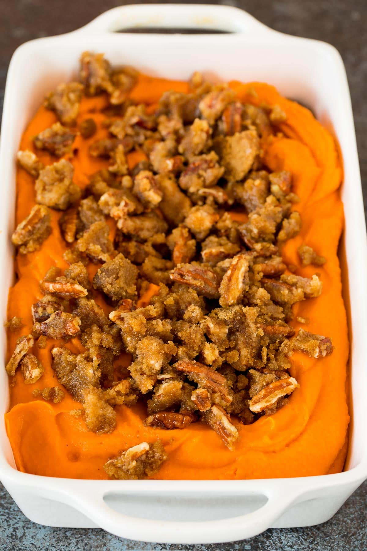 Pureed sweet potatoes in a dish with brown sugar and pecans on top.
