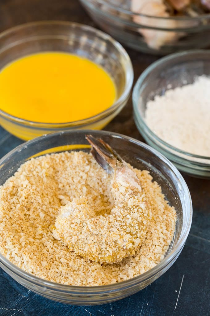 Bowls of egg, flour and breadcrumbs with a shrimp coated in crumbs.