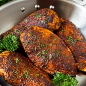 A pan of blackened chicken breasts garnished with fresh parsley.