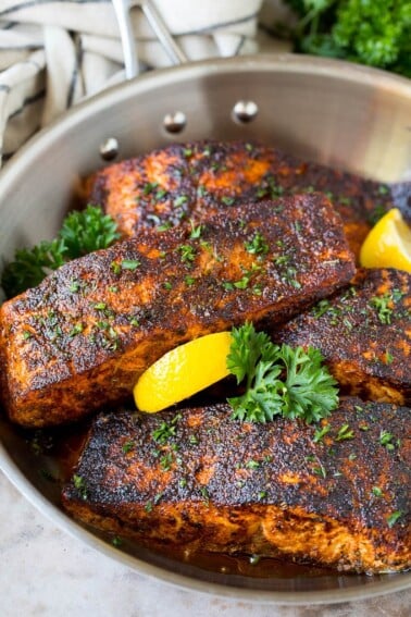 A pan of blackened salmon fillets garnished with lemon and parsley.