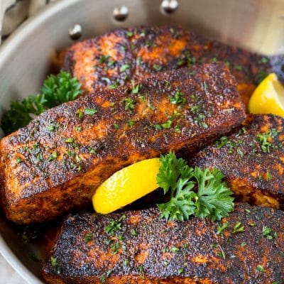 A pan of blackened salmon fillets garnished with lemon and parsley.