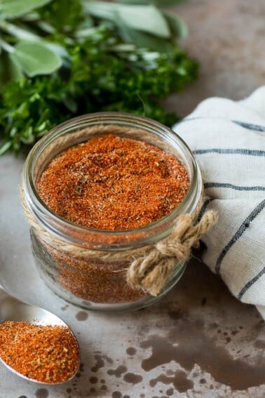 A jar of blackened seasoning with fresh herbs in the background.