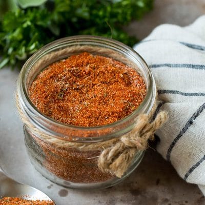 A jar of blackened seasoning with fresh herbs in the background.