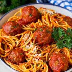 A serving bowl of crock pot spaghetti topped with meatballs and grated cheese.