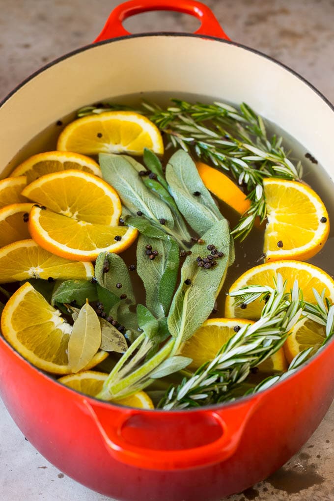 A pot of liquid with oranges, herbs and peppercorns.