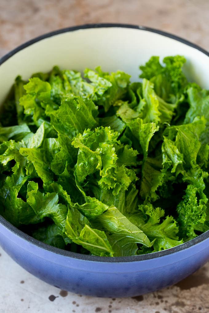 Torn leafy vegetables in a pot with bacon and onions.