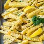 A sheet pan of roasted parsnips garnished with fresh parsley.