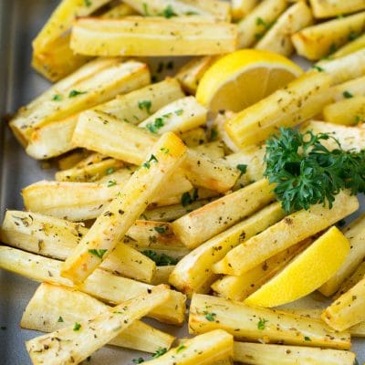 A sheet pan of roasted parsnips garnished with fresh parsley.