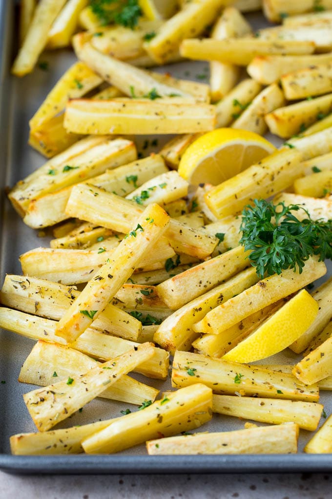 A sheet pan of roasted parsnips garnished with fresh parsley.