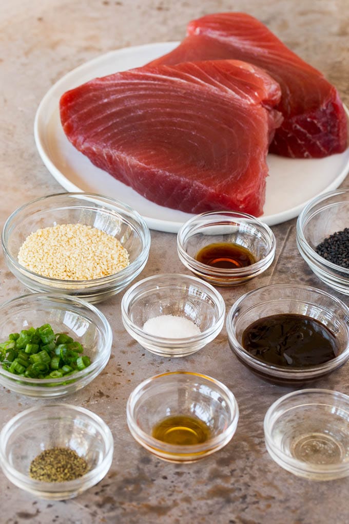 This seared ahi tuna recipe is sashimi grade fish coated in sesame seeds, then briefly cooked to tender and flavorful perfection. Bowls of ingredients and a plate of ahi tuna steaks.