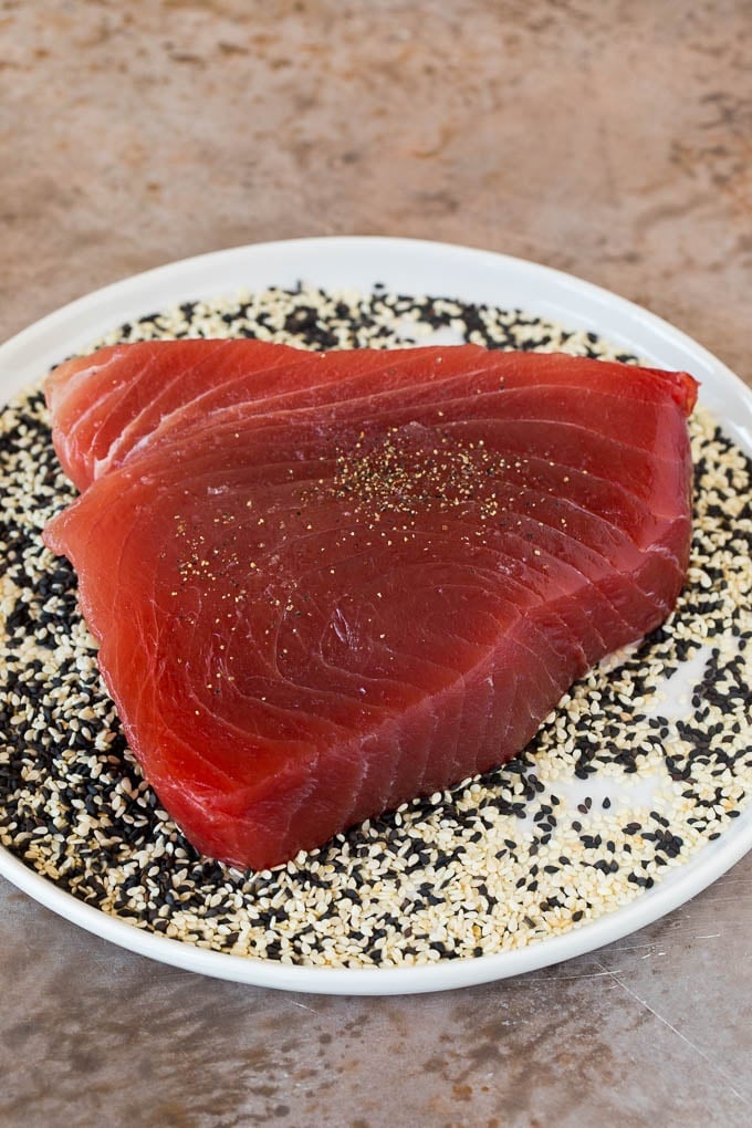This seared ahi tuna recipe is sashimi grade fish coated in sesame seeds, then briefly cooked to tender and flavorful perfection. A plate full of sesame seeds with a tuna steak on top.