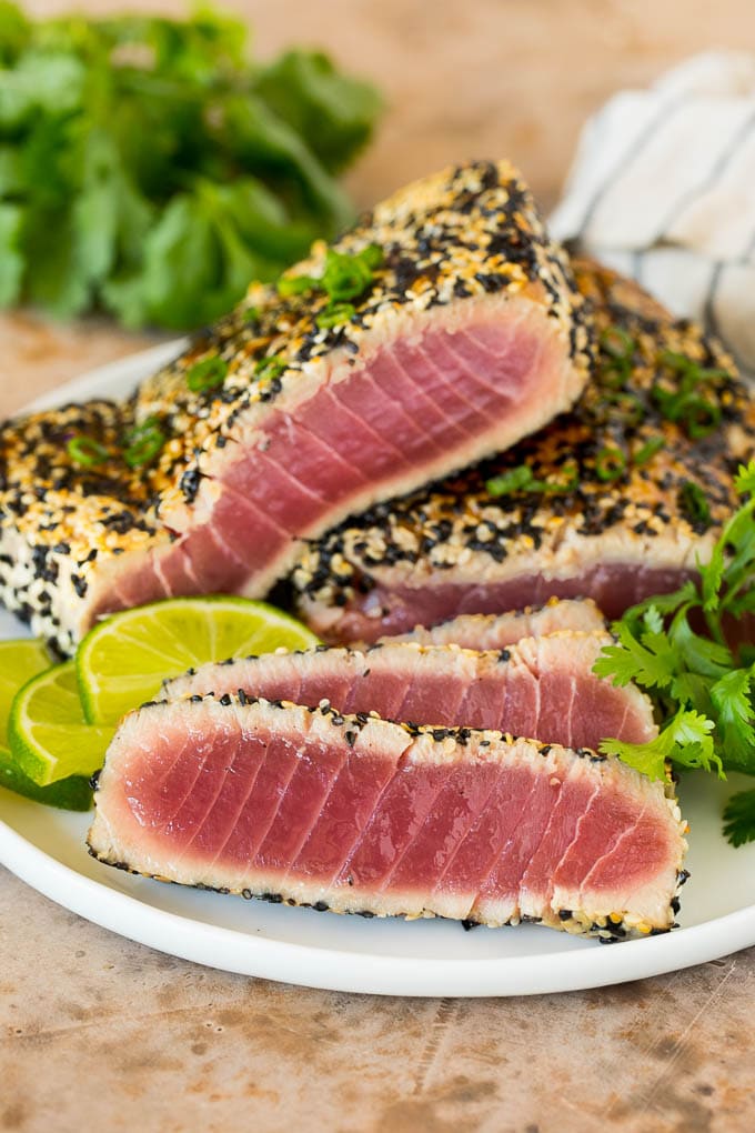 This seared ahi tuna recipe is sashimi grade fish coated in sesame seeds, then briefly cooked to tender and flavorful perfection. Seared ahi tuna fillets served with fresh herbs.