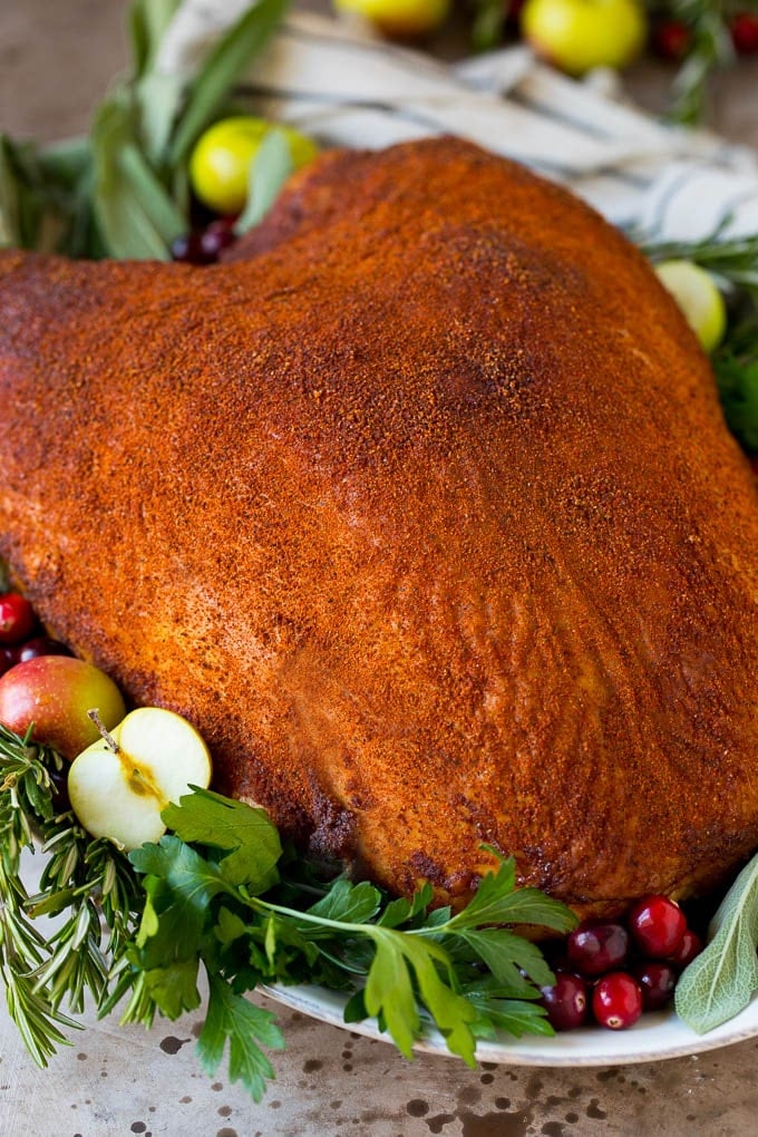 A smoked turkey breast on a platter garnished with fruit and herbs.