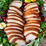 Sliced smoked turkey breast on a serving plate with herbs.