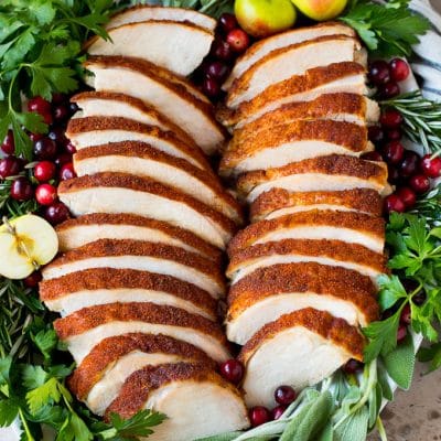 Sliced smoked turkey breast on a serving plate with herbs.